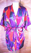 This is a short surplus wrap style robe from probably the 1970\'s. It has bright colors in a geometric print. There is a V neckline with no collar and short elbow length sleeves. There is a matching tie belt to cinch the waist. There is no lining. The fabric is silky poly. The label is no longer present and it is a one size fits all. Adjustable with the tie belt. 